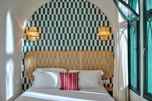 Un letto con lenzuola bianche e un cuscino a righe, una parete a quadri e due lampade fissate al muro.
