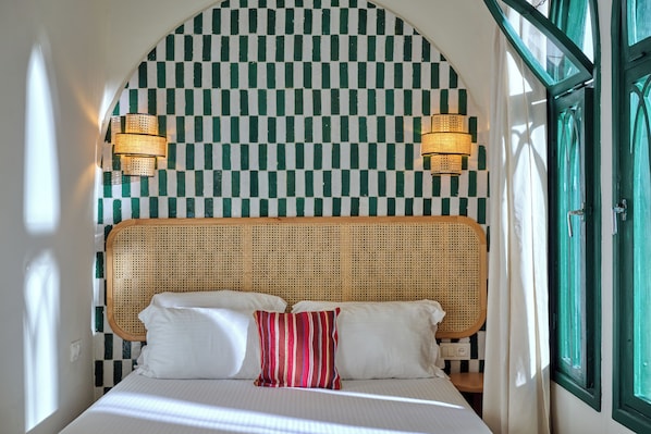 A bed with white linens and a single striped pillow, a checkered wall, and two wall-mounted lamps.