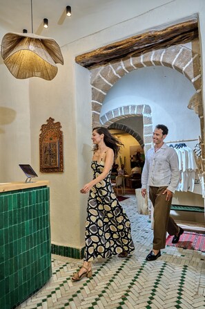 A hotel lobby with a reception desk, a patterned wall decoration, and a stone archway.