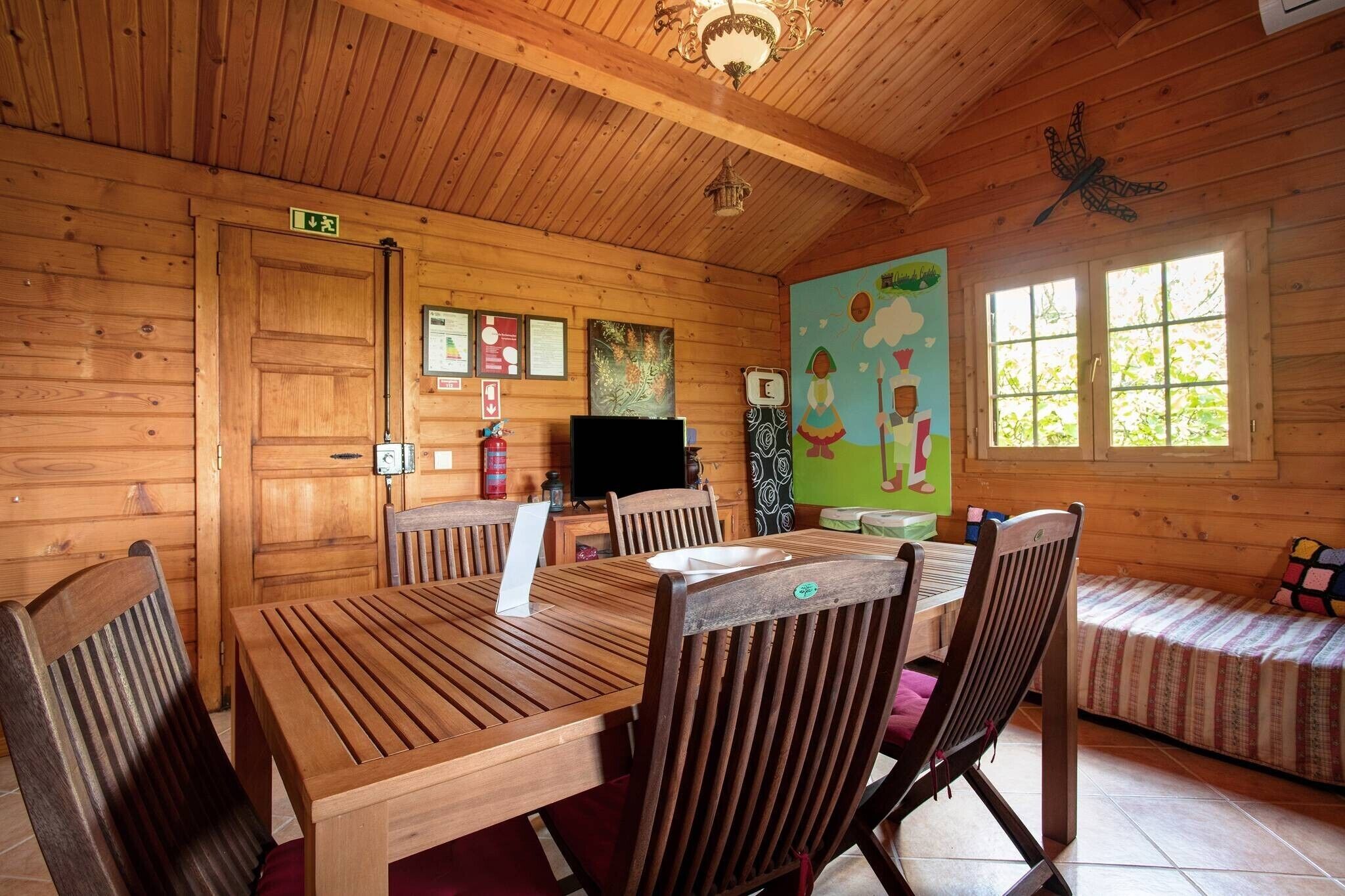 A wooden cabin interior with a dining table, chairs, a television, and a mural on the wall.