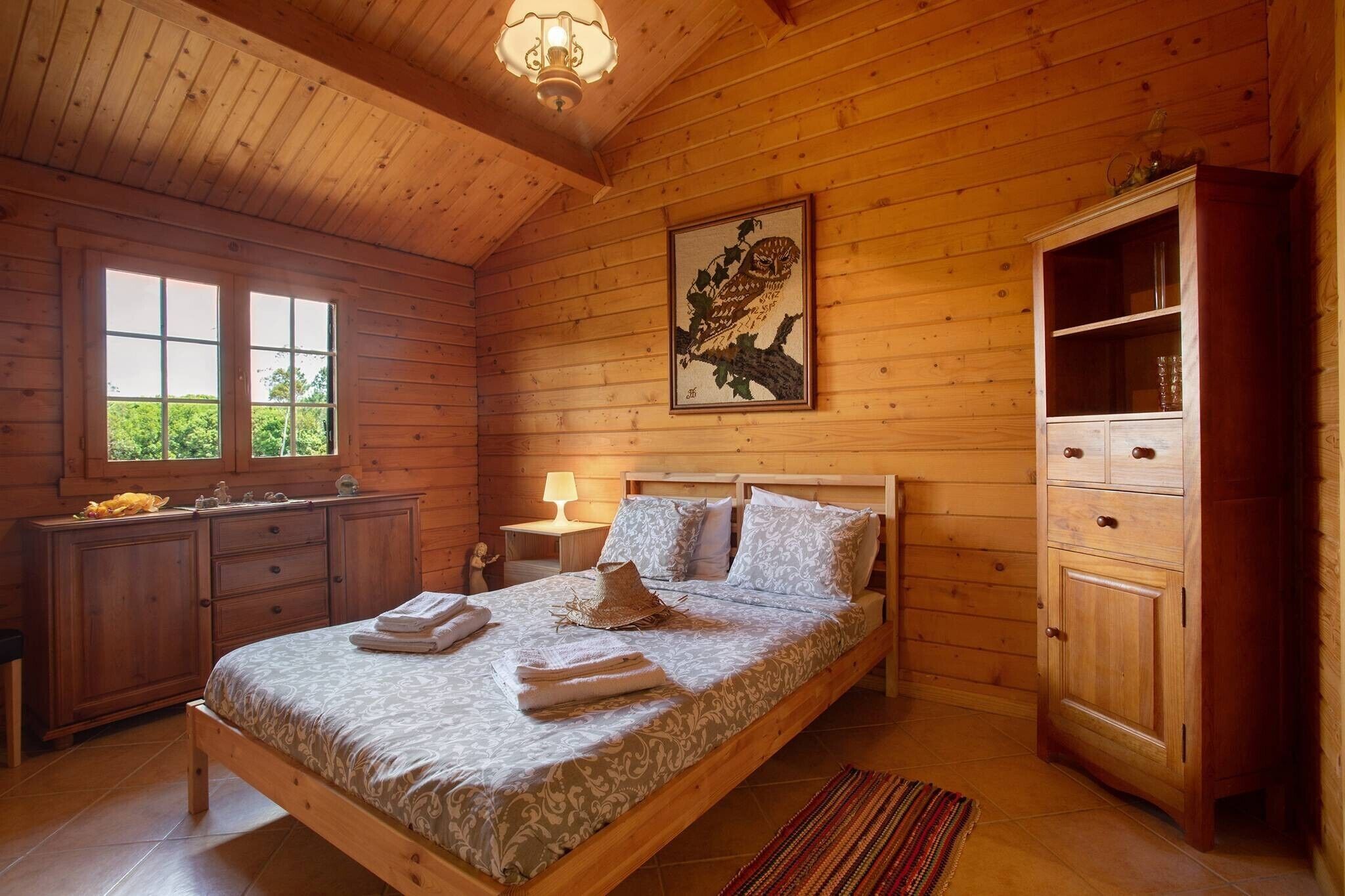 Una habitación con piso de madera, una cama, una mesita de noche, un aparador y una ventana.