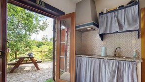 Una cocina con vistas a un jardín, una mesa de madera afuera y una cortina de cuadros.