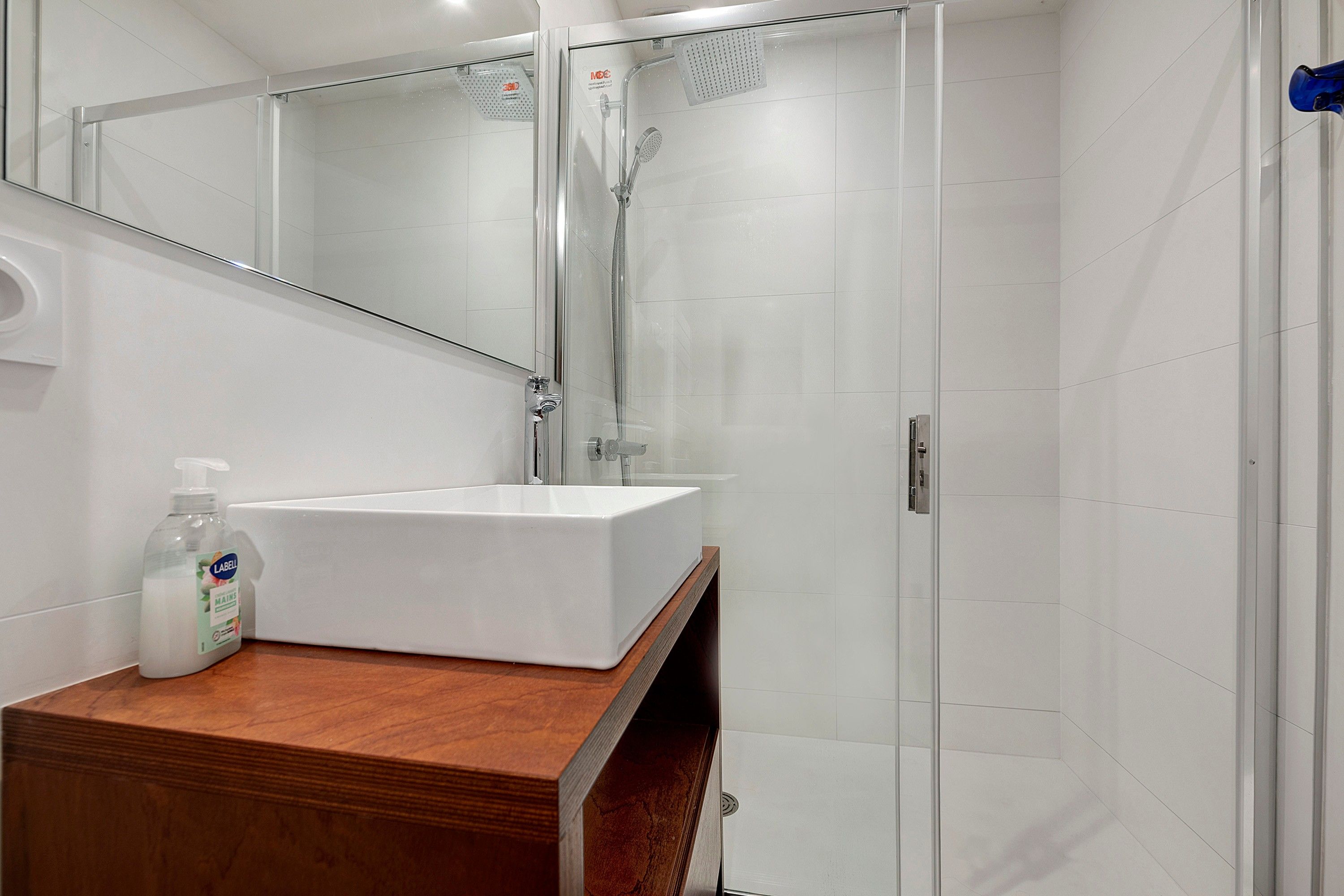A modern bathroom with a white sink, a mirror, and a shower enclosure.