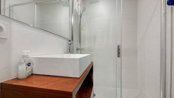 A modern bathroom with a white sink, a mirror, and a shower enclosure.