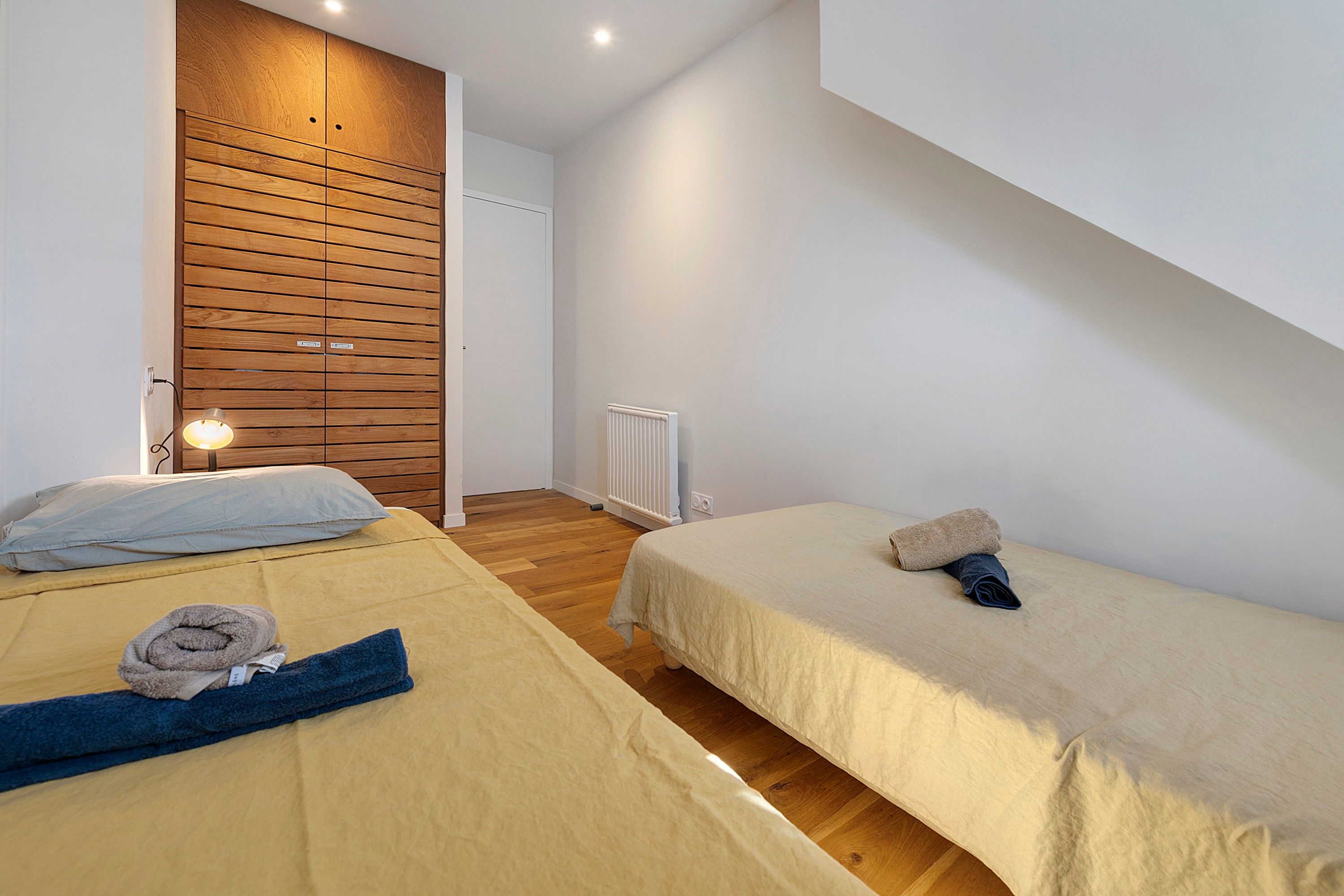 Ein Schlafzimmer mit zwei Betten, Holzwandverkleidung, einem Heizkörper und einer Leuchte.