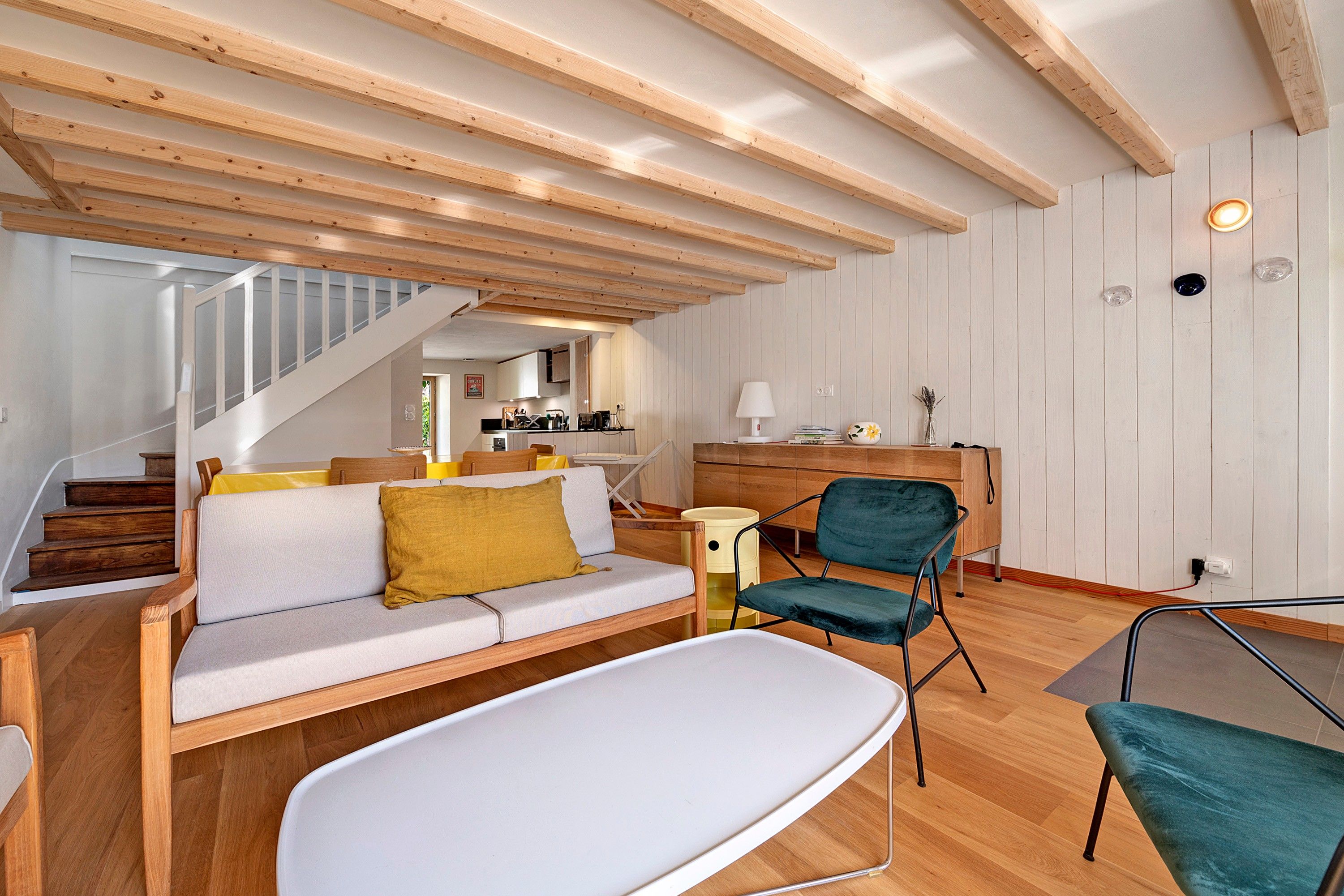 Ein modernes Interieur mit Holzboden, einer Couch mit Kissen, einem Esstisch und einem Stuhl.