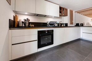 A modern kitchen with white cabinetry, a black oven, and a stainless steel coffee maker. - House 'Charmante maison' with Terrace, Garden and Wi-Fi near the Sea (Arzon)