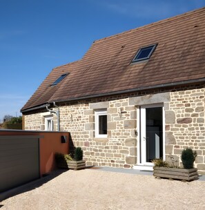 A stone building with a brown tiled roof, a white door, and a small window.