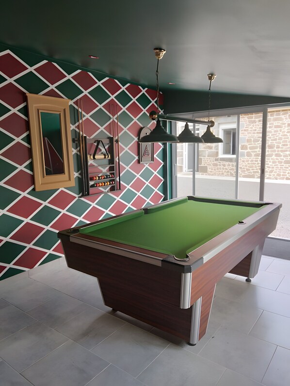 A pool table in a room with a geometric patterned wall, a framed picture, and a hanging light fixture.