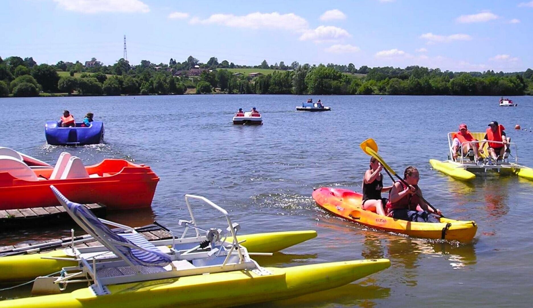 Een meer met verschillende waterfietsen, waaronder kayaks en roeiboten, wat wijst op een recreatiegebied.