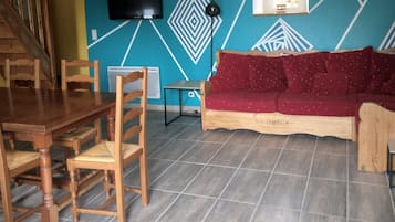 Un comedor con mesa y sillas de madera, un sofá con cojines rojos y una pared con diseños geométricos.