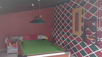 Een pooltafel met een groene viltkleed, een rode bank met kleurrijke kussens, en een muur met een diamantpatroon.