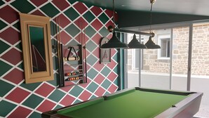 Een biljart in een kamer met een geometrisch behang, een ingelijst schilderij en een hanglamp.