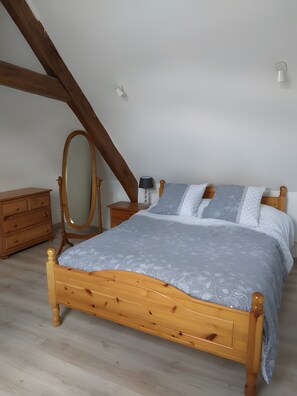 A bedroom with a wooden bed, a nightstand, a dresser, a mirror, and a lamp.