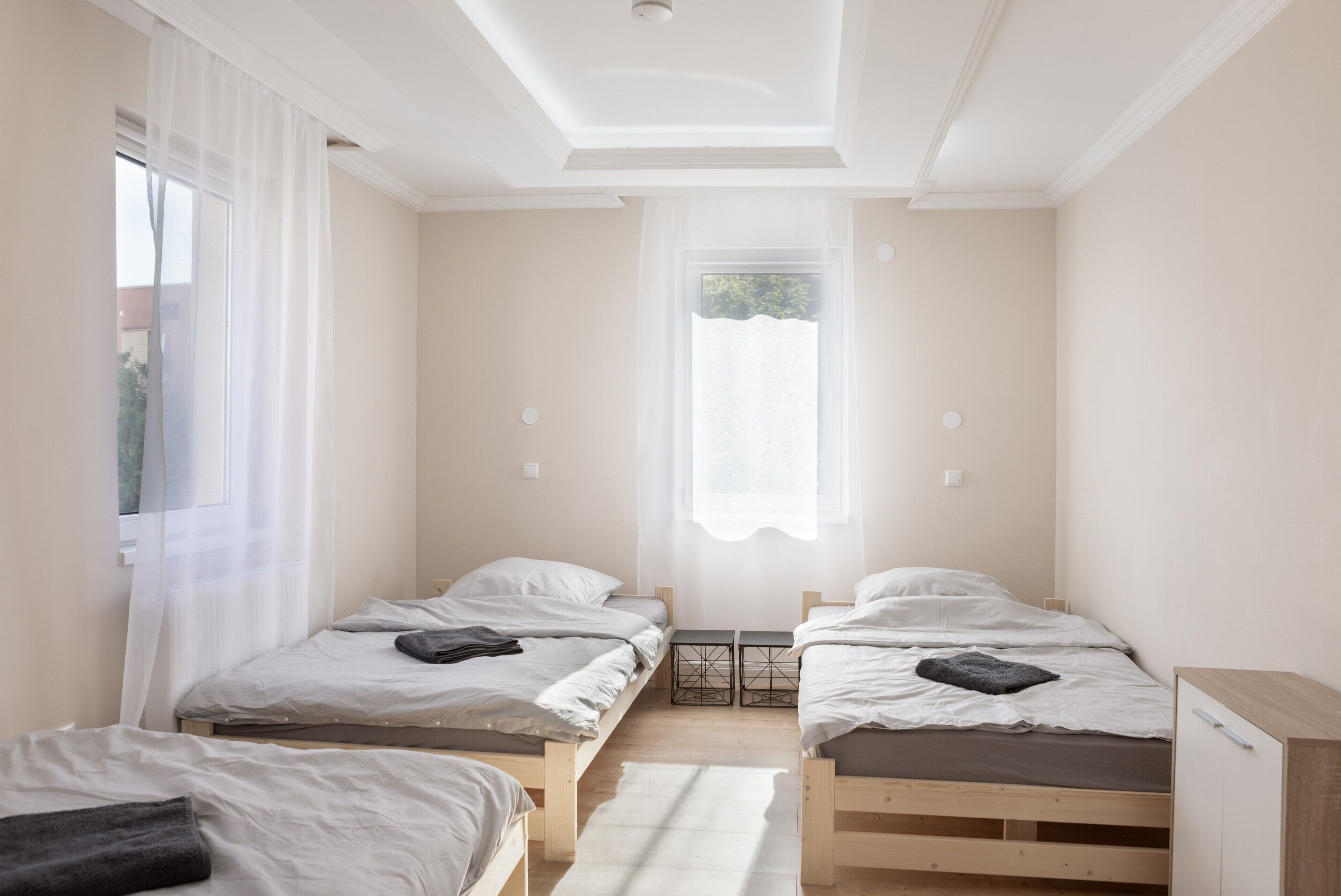 Ein Zimmer mit zwei Einzelbetten, einem kleinen Tisch und einem Fenster mit durchsichtigen Vorhängen.