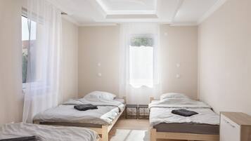 Ein Zimmer mit zwei Einzelbetten, einem kleinen Tisch und einem Fenster mit durchsichtigen Vorhängen.