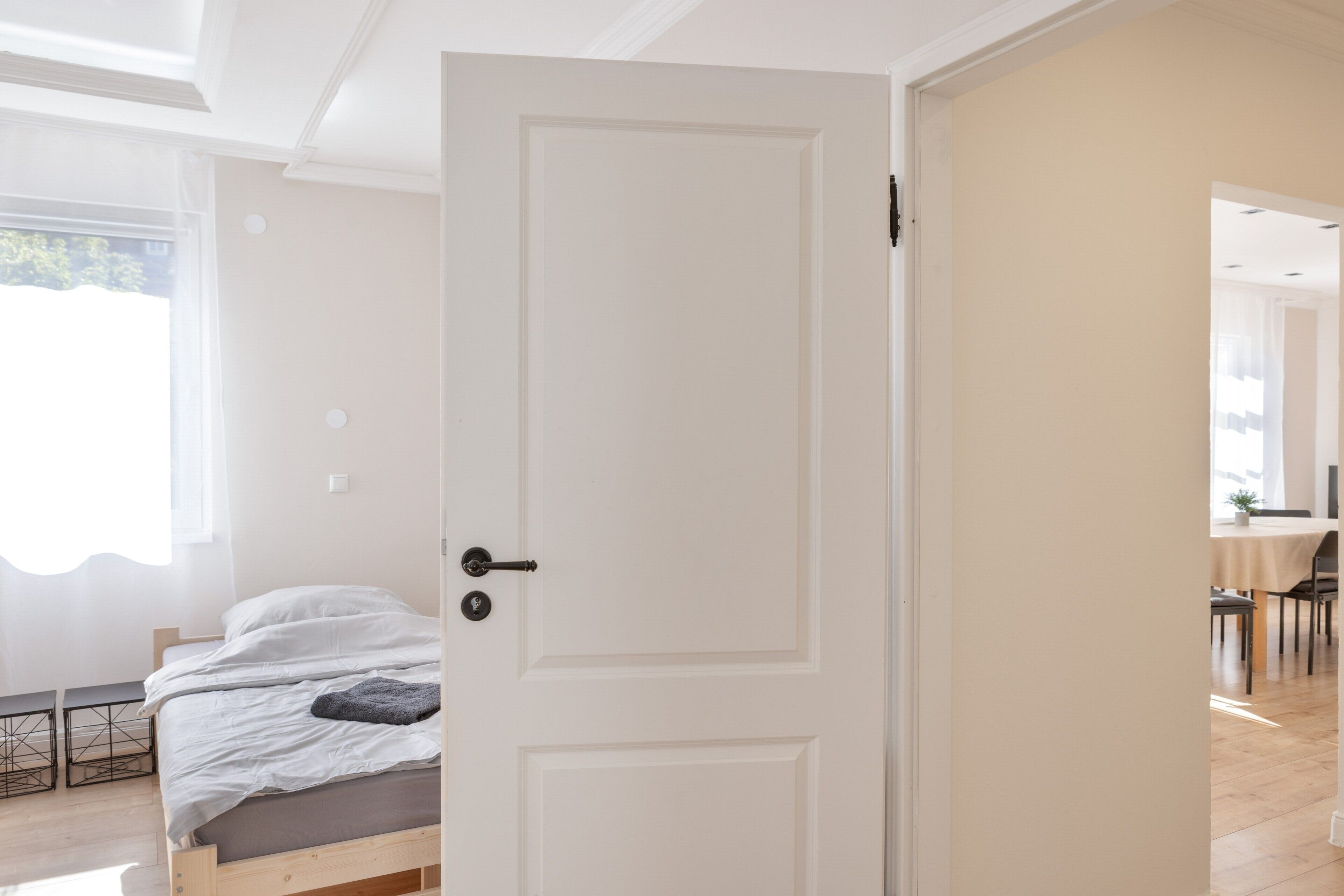 A room with a bed, a door, and a view of another room with a table and chairs.
