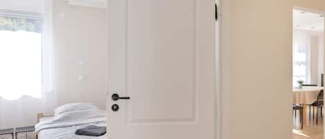 A room with a bed, a door, and a view of another room with a table and chairs.