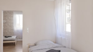 A small, single-bed room with a wooden floor, a bedside table, and a window with sheer curtains. - Apartment "C & D II" with Shared Terrace and Wi-Fi (Bad Kissingen)