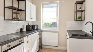 A modern kitchen with white cabinets, a black countertop, a built-in oven, a kettle, and a window with blinds. - Apartment "C & D II" with Shared Terrace and Wi-Fi (Bad Kissingen)
