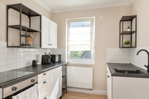 A modern kitchen with white cabinets, a black countertop, a built-in oven, a kettle, and a window with blinds. - Apartment "C & D II" with Shared Terrace and Wi-Fi (Bad Kissingen)