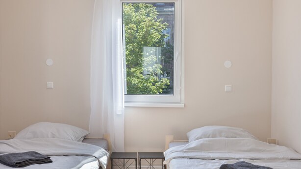 A bedroom with two beds, a window with a view of trees, and a white curtain. - Apartment "C & D II" with Shared Terrace and Wi-Fi (Bad Kissingen)