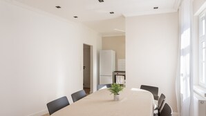 A modern dining room with a long table, chairs, a potted plant, and a view of a kitchen and bathroom through an open doorway. - Apartment "C & D II" with Shared Terrace and Wi-Fi (Bad Kissingen)