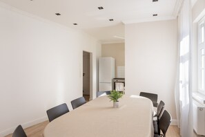 A modern dining room with a long table, chairs, a potted plant, and a view of a kitchen and bathroom through an open doorway. - Apartment "C & D II" with Shared Terrace and Wi-Fi (Bad Kissingen)