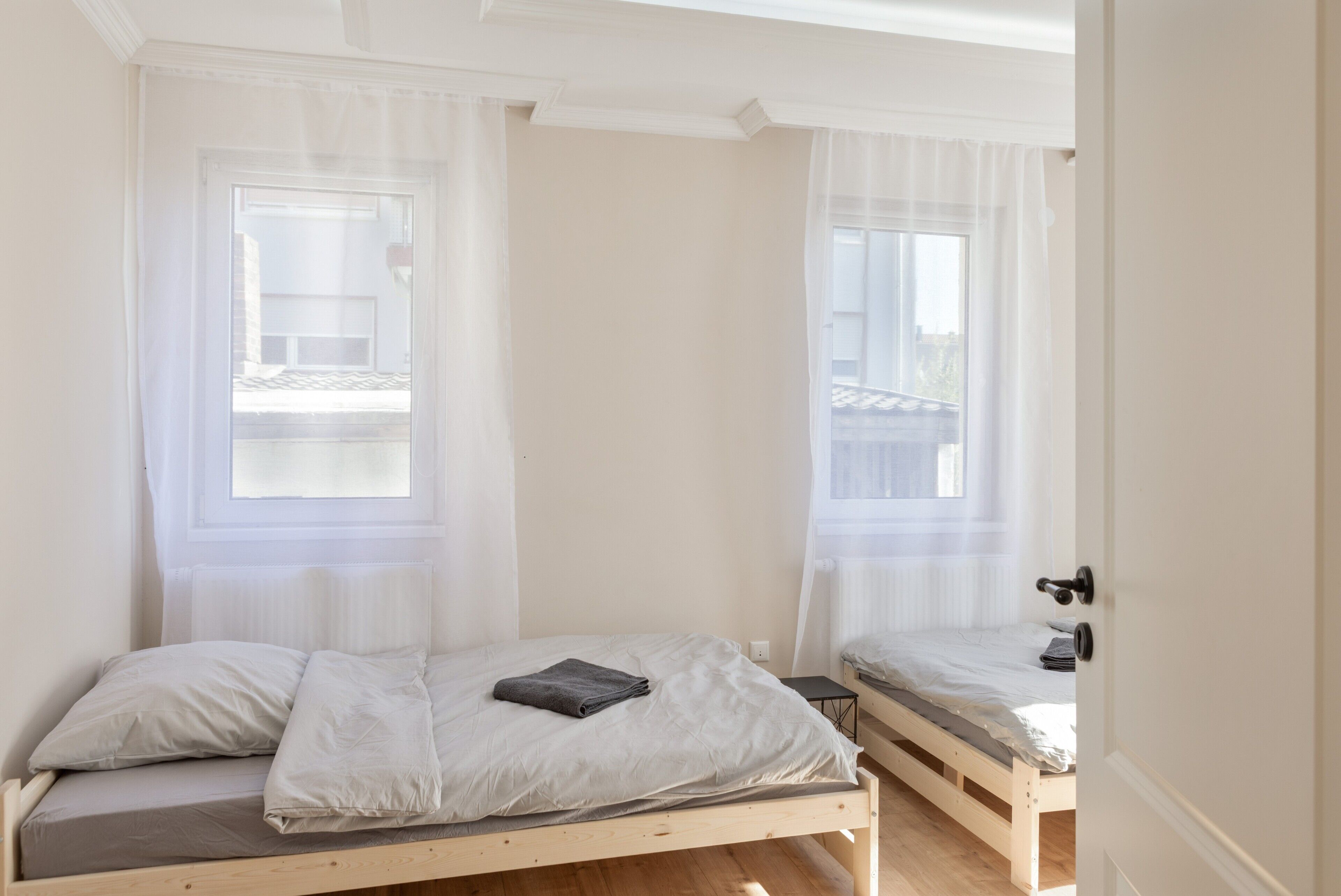 A bedroom with two single beds, a window with sheer curtains, and a door with a handle.