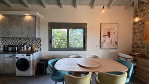 A modern kitchen with a built-in washing machine, a dining table with chairs, and a large window with a view of greenery. - Panoramic Sea View Villa near Galaxidi (Gerakofono Galaxidi)