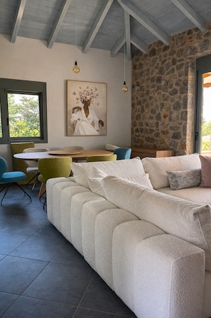 A modern living room with a stone wall, a sofa, a dining table with chairs, and a hanging light fixture. - Panoramic Sea View Villa near Galaxidi (Gerakofono Galaxidi)
