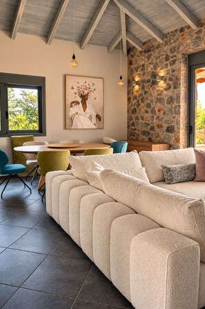 A modern living room with a sofa, a dining table, chairs, and a stone wall. - Panoramic Sea View Villa near Galaxidi (Gerakofono Galaxidi)