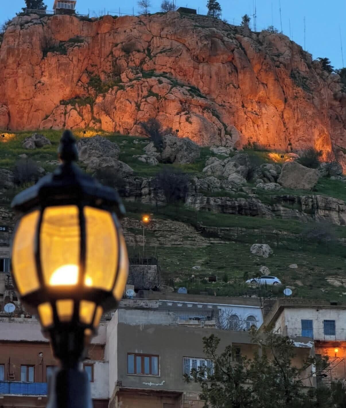 Paisaje montañoso con un risco rocoso y una edificación al frente.