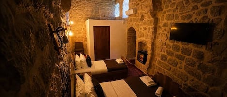 A stone-walled room with a bed, a wooden door, a flat-screen TV, and a fireplace.