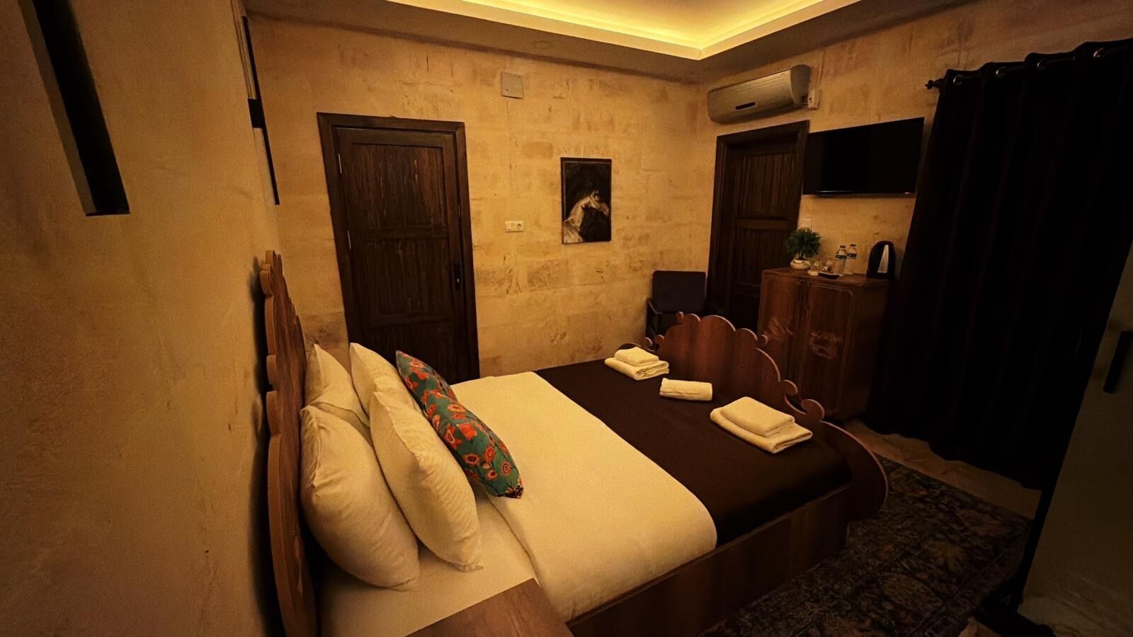 Une chambre d’hôtel avec un lit, une tête de lit en bois, un téléviseur à écran plat, un appareil de climatisation et un rideau foncé.