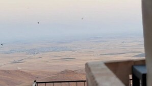 Une vue depuis un balcon, avec un ciel dégagé, un paysage lointain et quelques oiseaux.