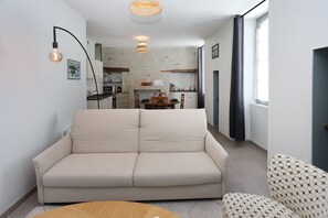 Ein Wohnzimmer mit einer Couch, einem Esstisch und einer Küche im Hintergrund.