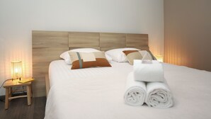 Una cama bien hecha con cabecera de madera, una mesita de noche con una lámpara y toallas enrolladas sobre la cama.