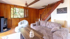 Ein gemütliches Wohnzimmer mit Holzvertäfelung, einer Couch, einem Sessel, einem Holztisch, einem Kamin und einer Treppe.