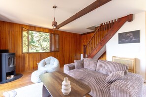 Ein gemütliches Wohnzimmer mit Holzvertäfelung, einer Couch, einem Sessel, einem Holztisch, einem Kamin und einer Treppe.