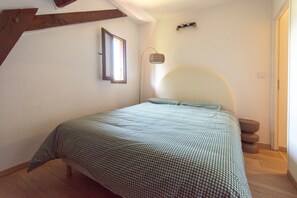 Une chambre à coucher avec un lit, une fenêtre, une lampe fixée au mur et un escalier en bois.