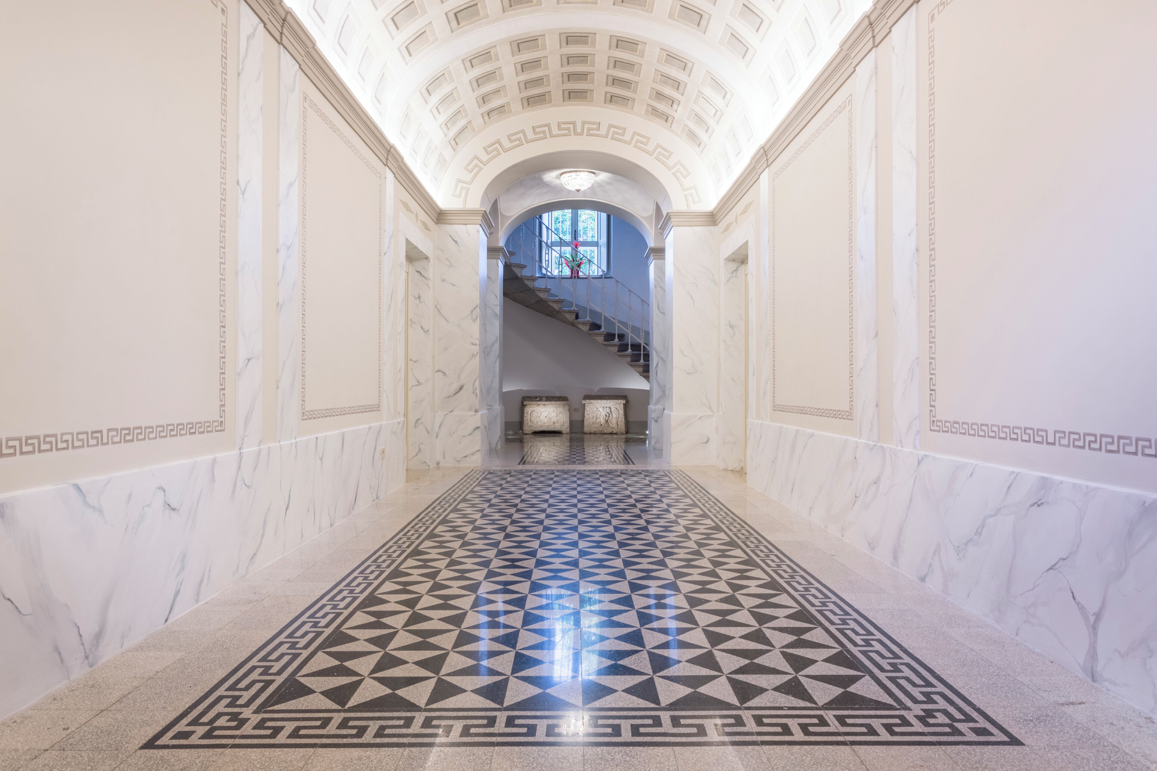 A marble-floored corridor with a geometric pattern leading to a staircase.