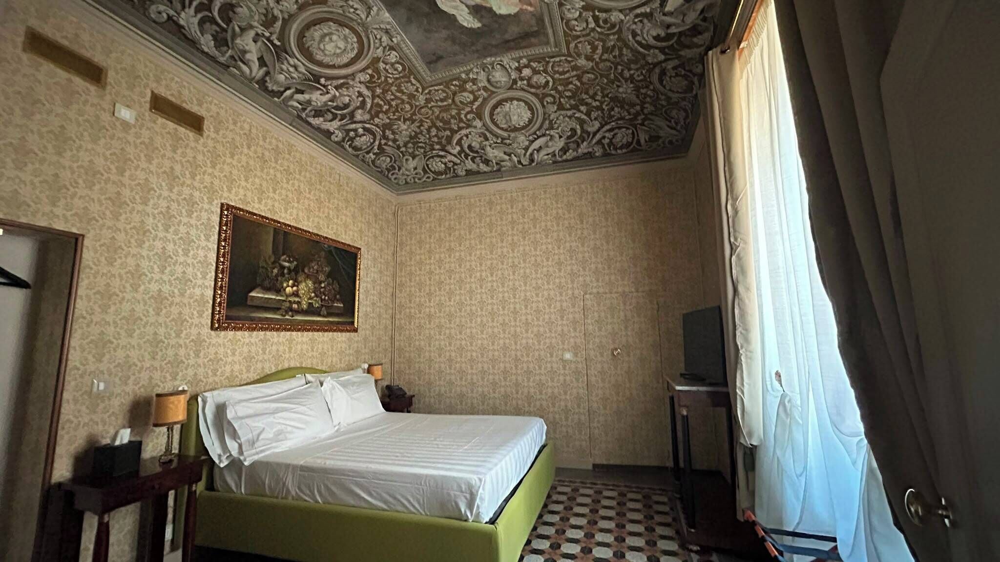 A hotel room with a bed, a painting, a television, and a patterned floor.