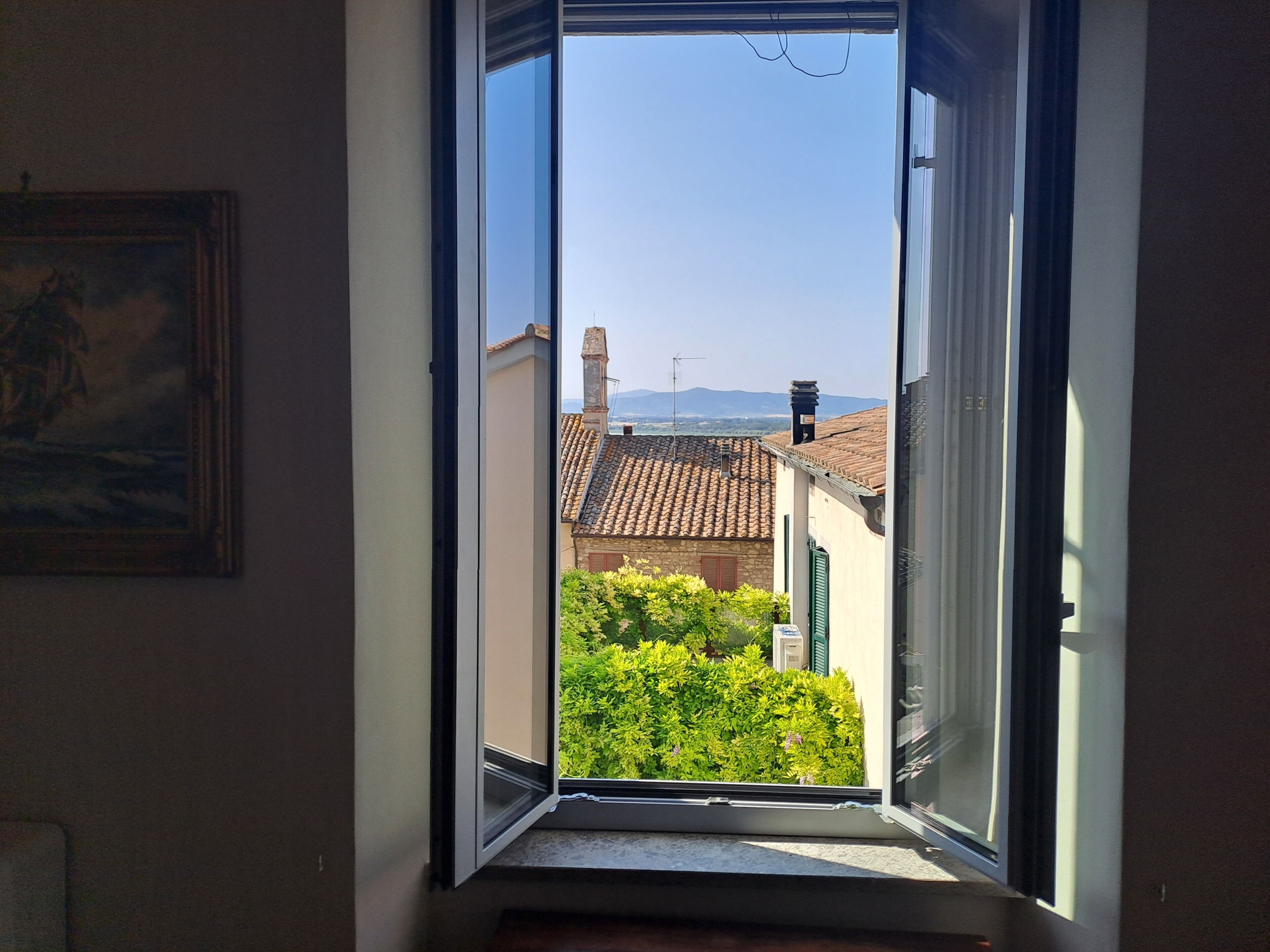 An open window with a view of a building with a tiled roof and greenery outside.