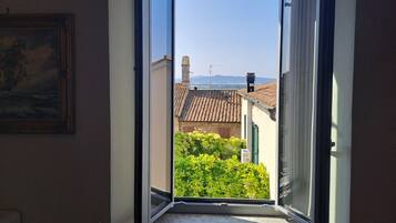 Una ventana abierta con vista a un edificio de techo de tejas y vegetación.