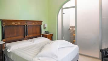 A hotel room with a wooden headboard, a bed with white linens, a bedside telephone, and a sliding glass door leading to a bathroom.