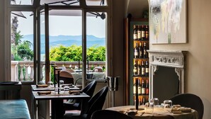 A dining area with a view of mountains, a chandelier, and a wine rack. - Garden Palace Hotel (Castiglione del Lago)