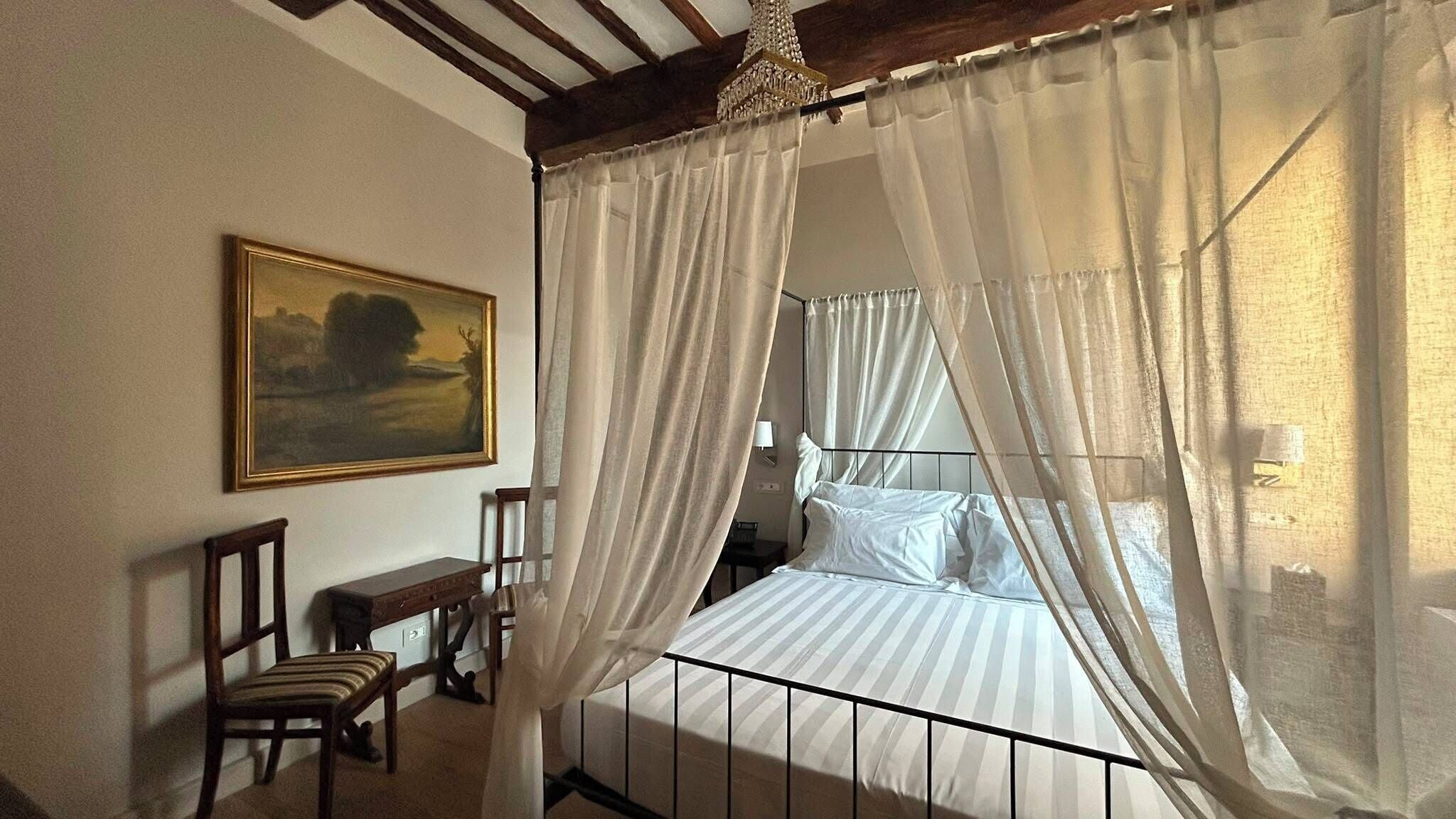 Un dormitorio con una cama con dosel, una mesita de noche, una silla y un cuadro en la pared.