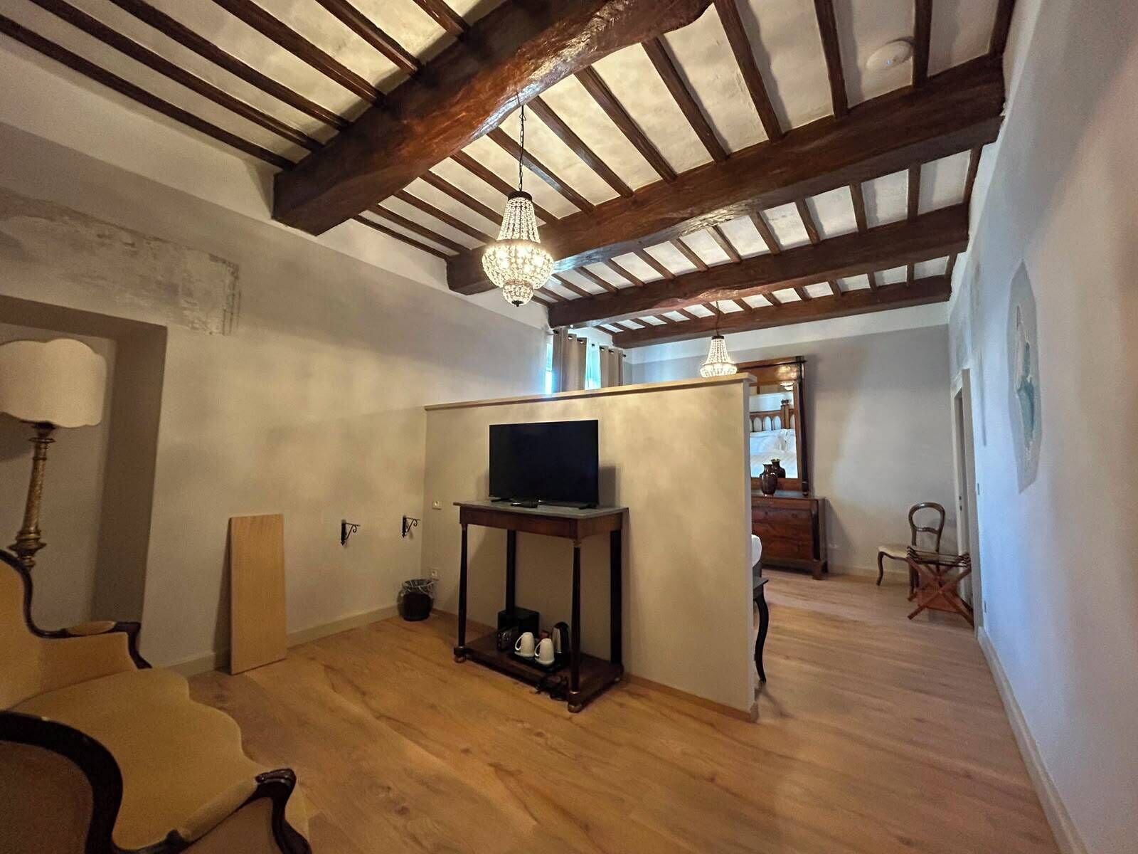A room with exposed wooden beams, a television on a stand, a chandelier, and a chair.