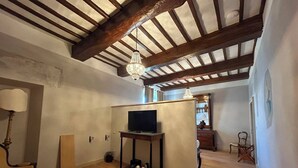 A room with exposed wooden beams, a television on a stand, a chandelier, and a chair. - Garden Palace Hotel (Castiglione del Lago)